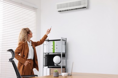 Image of Woman using remote to control air conditioner in office