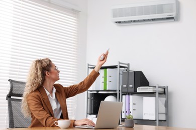 Image of Woman using remote to control air conditioner in office
