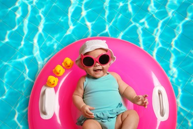 Image of Cute little baby with inflatable ring in swimming pool, top view
