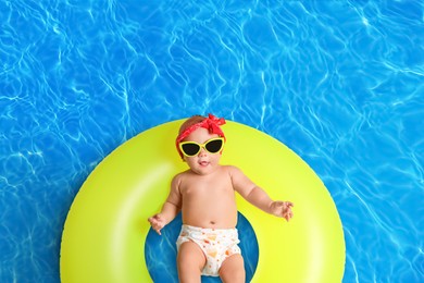 Image of Cute little baby with inflatable ring in swimming pool, top view