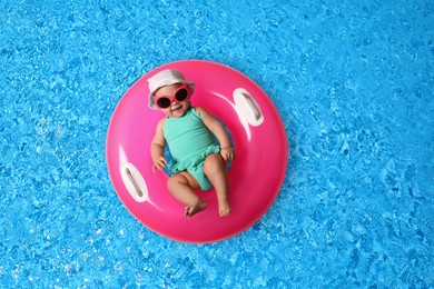 Image of Cute little baby with inflatable ring in swimming pool, top view