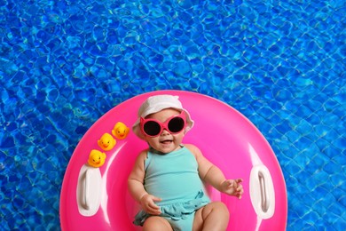 Image of Cute little baby with inflatable ring in swimming pool, top view