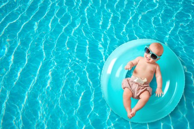 Image of Cute little baby with inflatable ring in swimming pool, top view