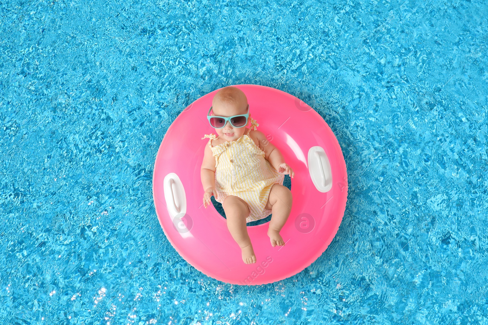 Image of Cute little baby with inflatable ring in swimming pool, top view