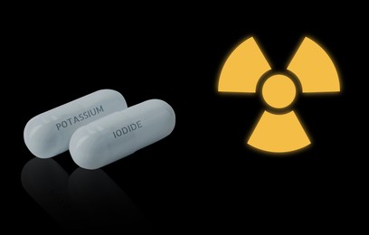 Image of Potassium iodide pills and warning sign on black background. Iodine consumption during radioactive contamination