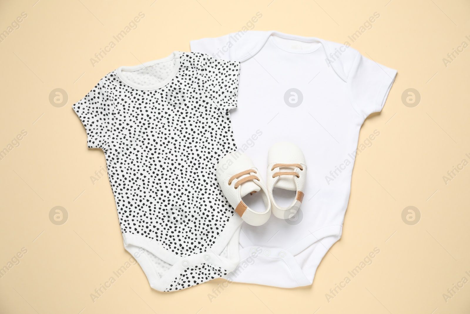 Stylish baby onesies and shoes on beige background, flat lay Photo of Stylish baby onesies and shoes on beige background, flat lay