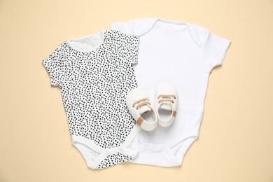 Photo of Stylish baby onesies and shoes on beige background, flat lay