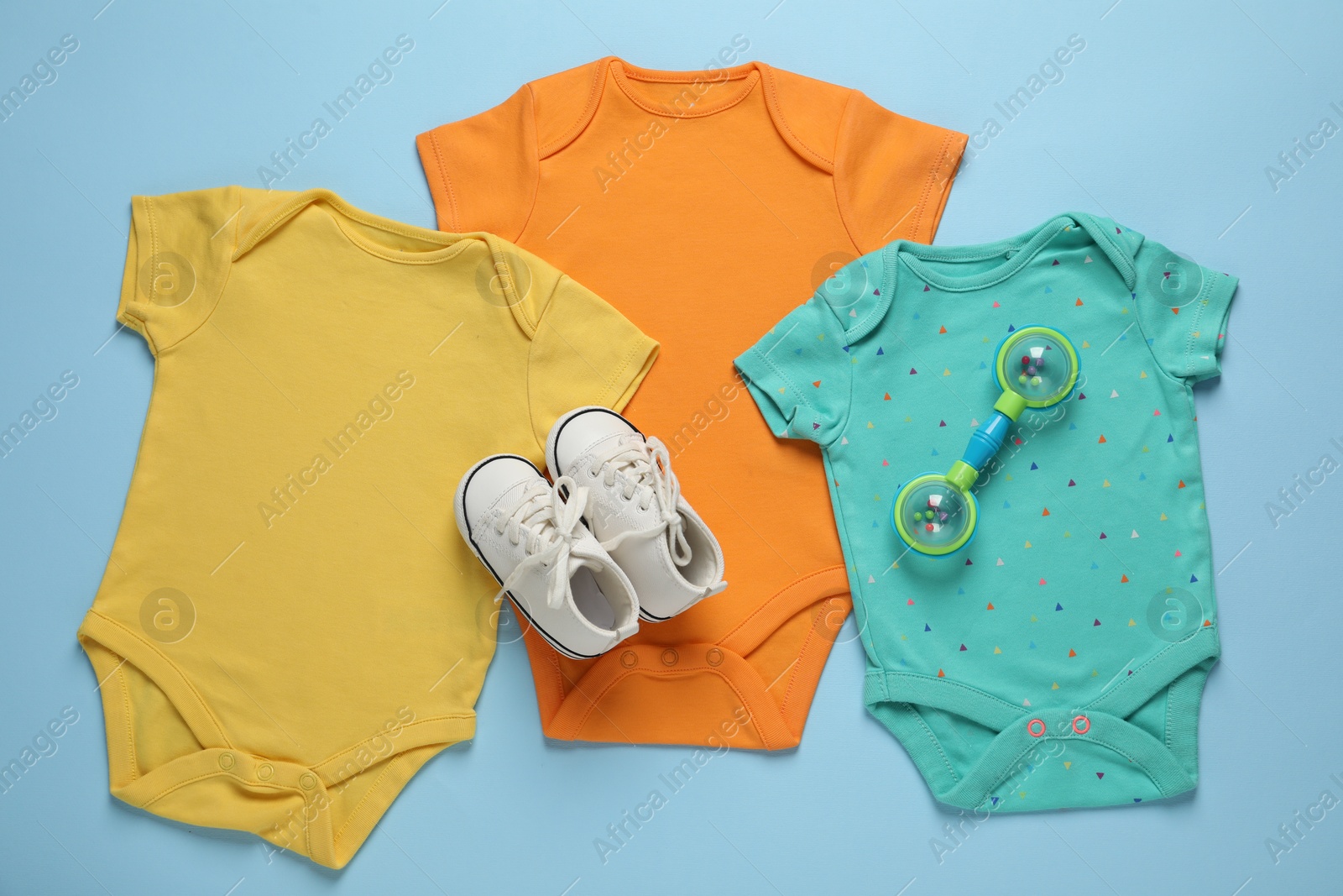 Photo of Stylish baby onesies and accessories on light blue background, flat lay