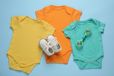 Photo of Stylish baby onesies and accessories on light blue background, flat lay