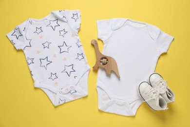 Photo of Stylish baby onesies and accessory on yellow background, flat lay