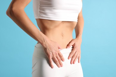 Photo of Woman doing abdominal vacuum exercise on light blue background, closeup