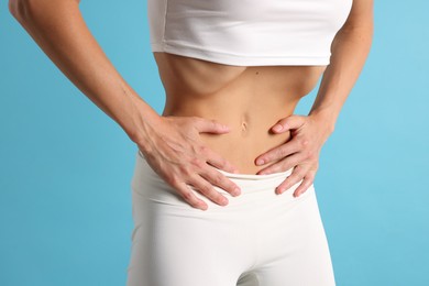 Photo of Woman doing abdominal vacuum exercise on light blue background, closeup