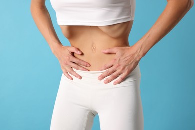 Photo of Woman doing abdominal vacuum exercise on light blue background, closeup