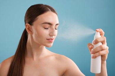 Photo of Beautiful woman spraying thermal water onto her face on light blue background