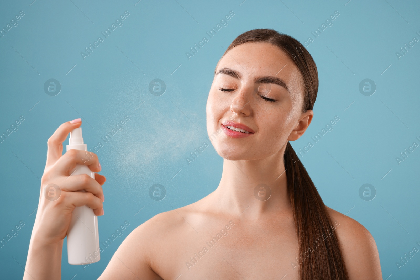 Smiling woman spraying thermal water onto her face on light blue background Photo of Smiling woman spraying thermal water onto her face on light blue background