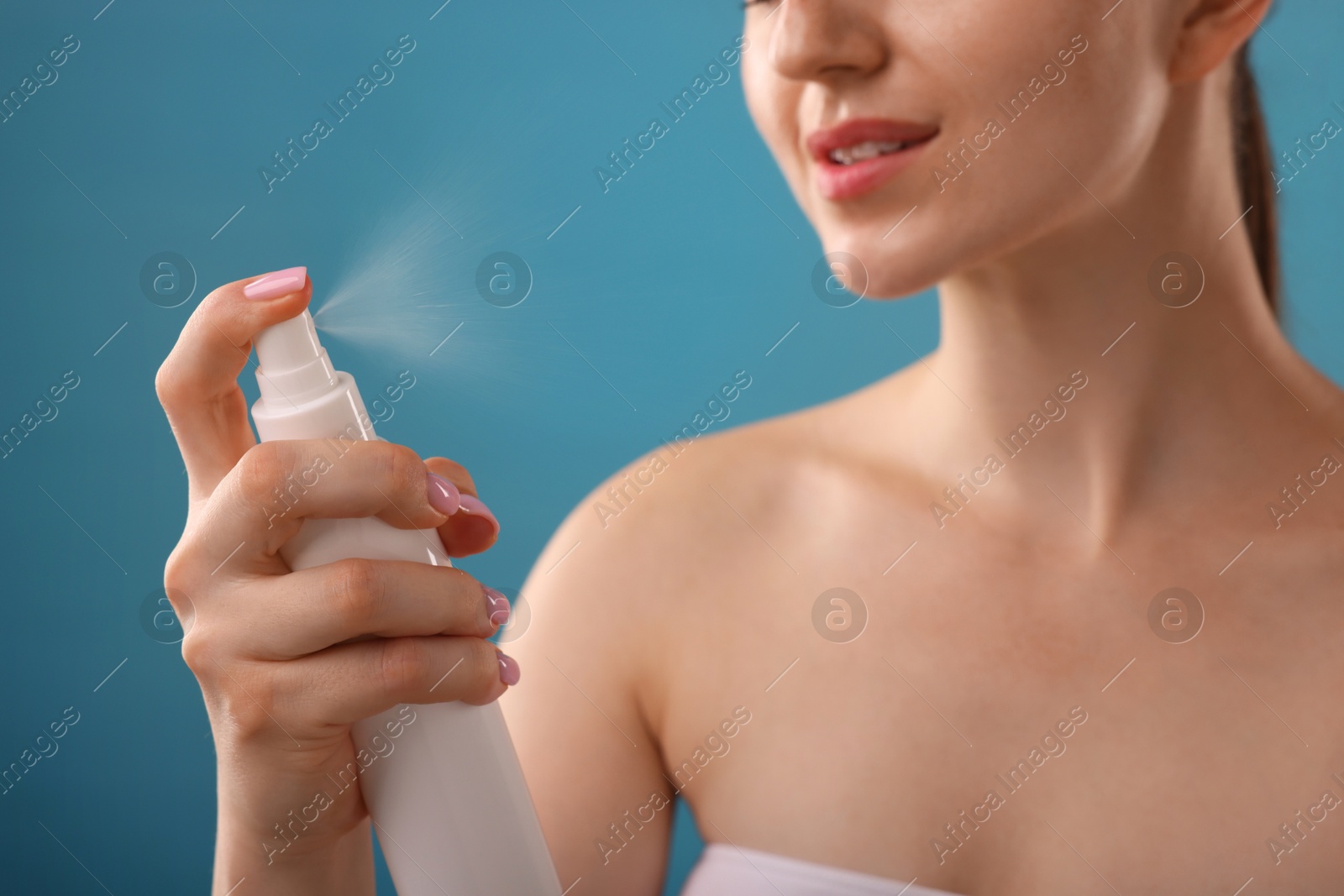 Woman spraying thermal water on light blue background, closeup Photo of Woman spraying thermal water on light blue background, closeup