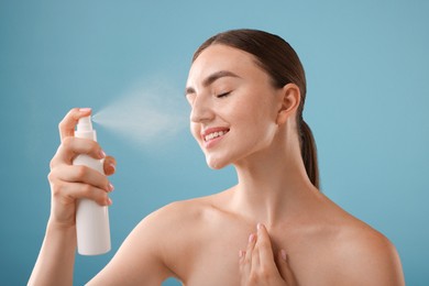 Photo of Smiling woman spraying thermal water onto her face on light blue background