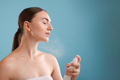 Photo of Beautiful woman spraying thermal water onto her neck on light blue background. Space for text