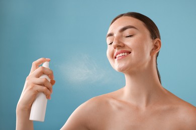Photo of Smiling woman spraying thermal water onto her face on light blue background