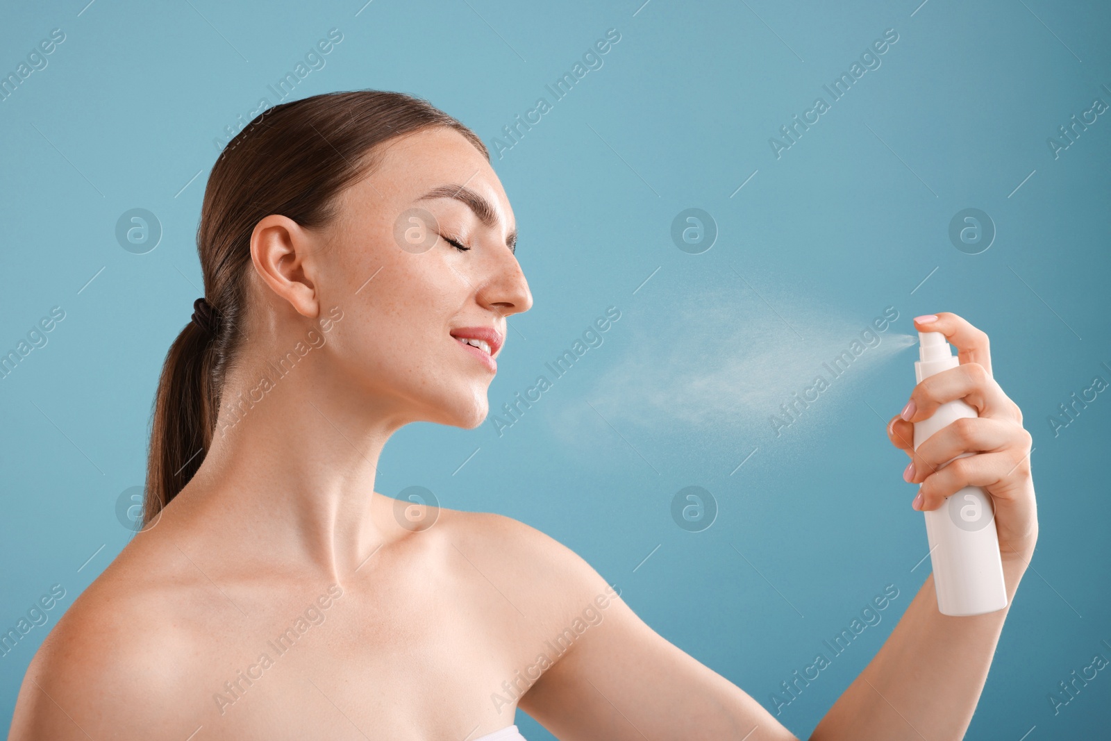 Smiling woman spraying thermal water onto her face on light blue background Photo of Smiling woman spraying thermal water onto her face on light blue background