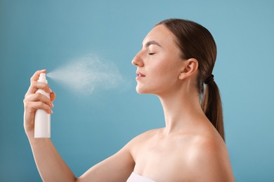 Photo of Beautiful woman spraying thermal water onto her face on light blue background