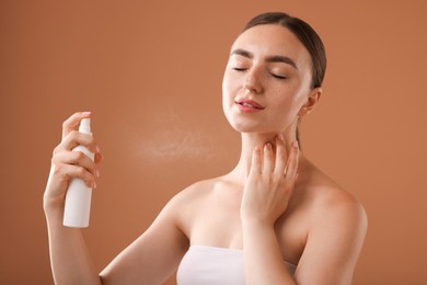 Photo of Beautiful woman spraying thermal water onto her neck on light brown background