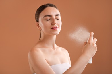 Photo of Beautiful woman spraying thermal water on light brown background