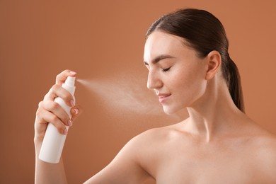 Photo of Beautiful woman spraying thermal water on light brown background