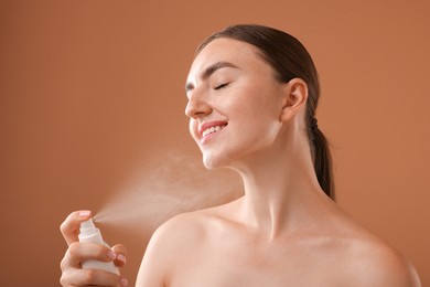 Photo of Smiling woman spraying thermal water onto her neck on light brown background