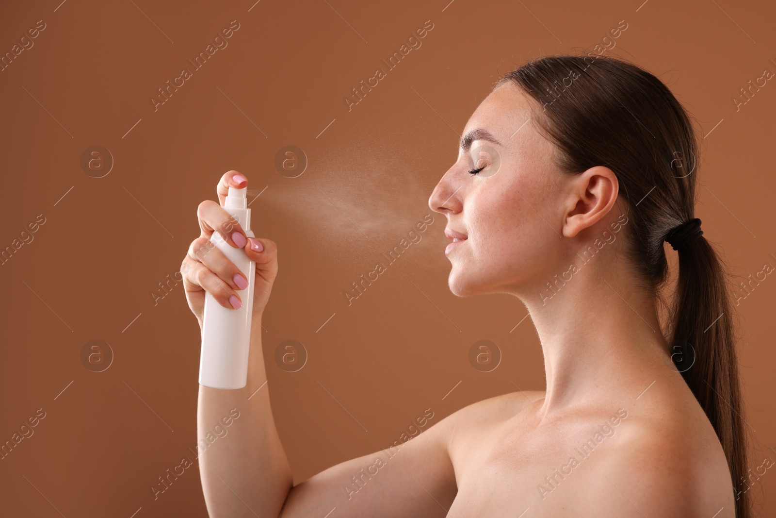 Beautiful woman spraying thermal water onto face on light brown background Photo of Beautiful woman spraying thermal water onto face on light brown background