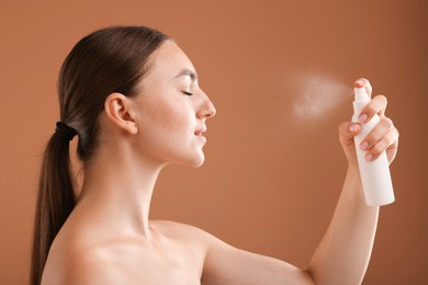 Photo of Beautiful woman spraying thermal water onto face on light brown background