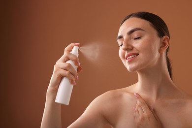 Photo of Smiling woman spraying thermal water onto her face on light brown background