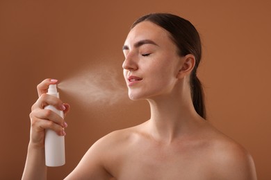 Photo of Beautiful woman spraying thermal water onto face on light brown background