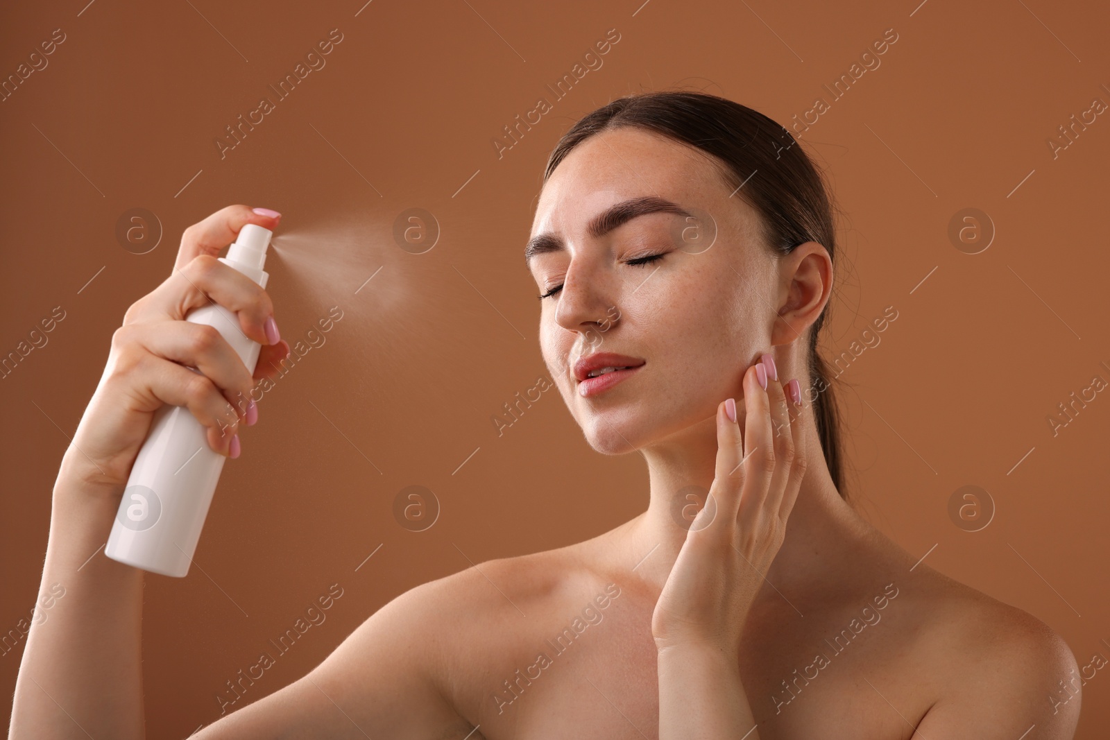 Beautiful woman spraying thermal water onto face on light brown background Photo of Beautiful woman spraying thermal water onto face on light brown background