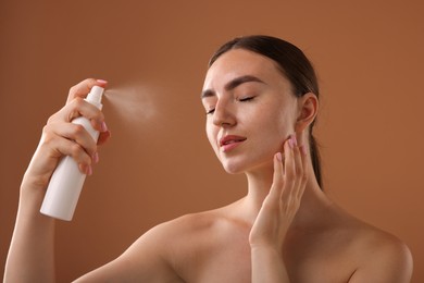 Photo of Beautiful woman spraying thermal water onto face on light brown background