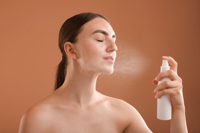 Photo of Beautiful woman spraying thermal water onto face on light brown background