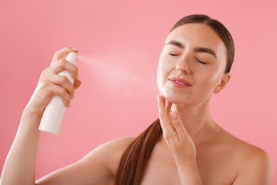 Photo of Beautiful woman spraying thermal water onto her face on pink background