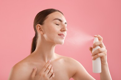 Photo of Beautiful woman spraying thermal water onto her face on pink background