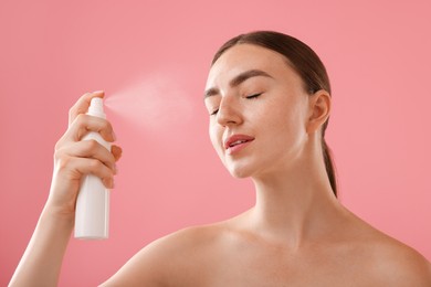 Photo of Beautiful woman spraying thermal water onto her face on pink background