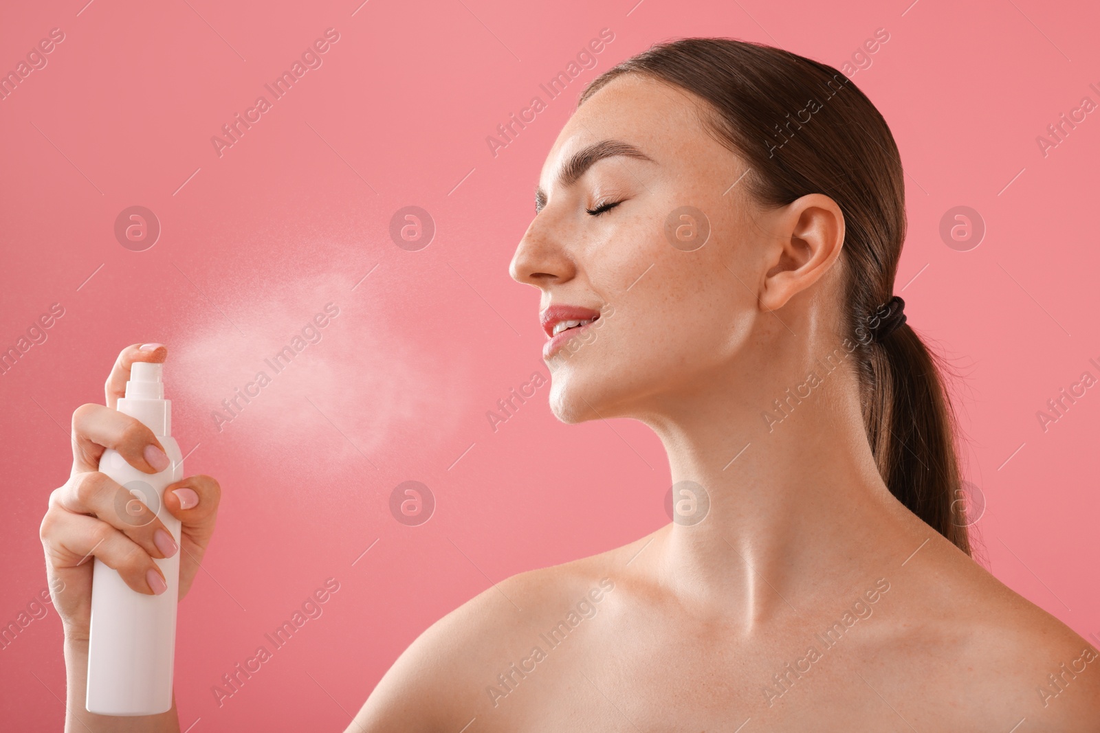 Beautiful woman spraying thermal water onto her face on pink background Photo of Beautiful woman spraying thermal water onto her face on pink background