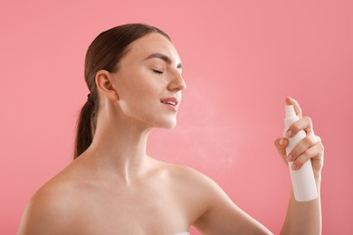 Photo of Beautiful woman spraying thermal water onto her face on pink background