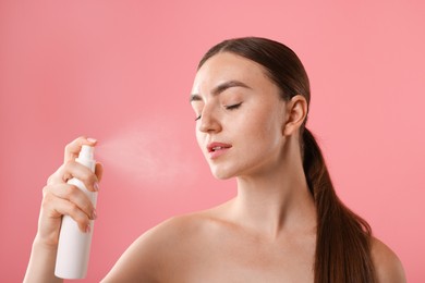 Photo of Beautiful woman spraying thermal water onto her face on pink background