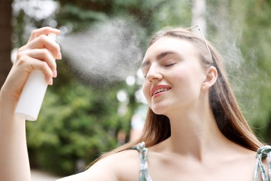 Photo of Smiling woman spraying thermal water onto her face outdoors