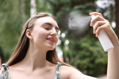 Photo of Smiling woman spraying thermal water onto her face outdoors