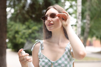 Photo of Smiling woman in sunglasses spraying thermal water onto her body outdoors