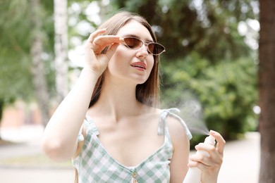 Photo of Smiling woman in sunglasses spraying thermal water onto her body outdoors