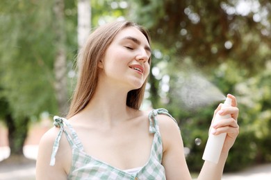 Photo of Smiling woman spraying thermal water onto her face outdoors