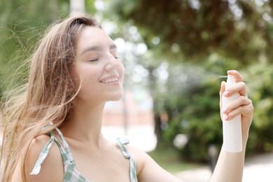 Photo of Smiling woman spraying thermal water onto her face outdoors
