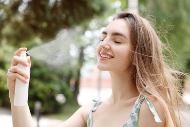 Photo of Smiling woman spraying thermal water onto her face outdoors