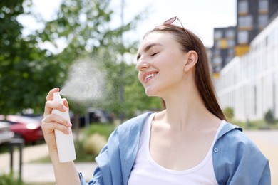 Photo of Smiling woman spraying thermal water onto her face outdoors